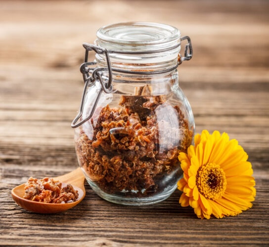 Propolis granule in glass jar on rustic wooden background